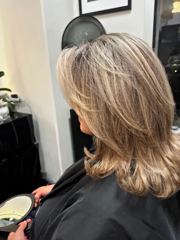 A client checks a fresh layered cut and golden color in a hand mirror